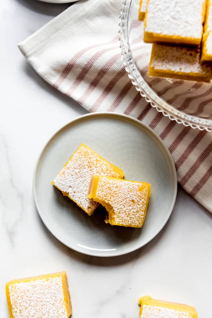 two lemon bars on a plate with a bite taken out of one