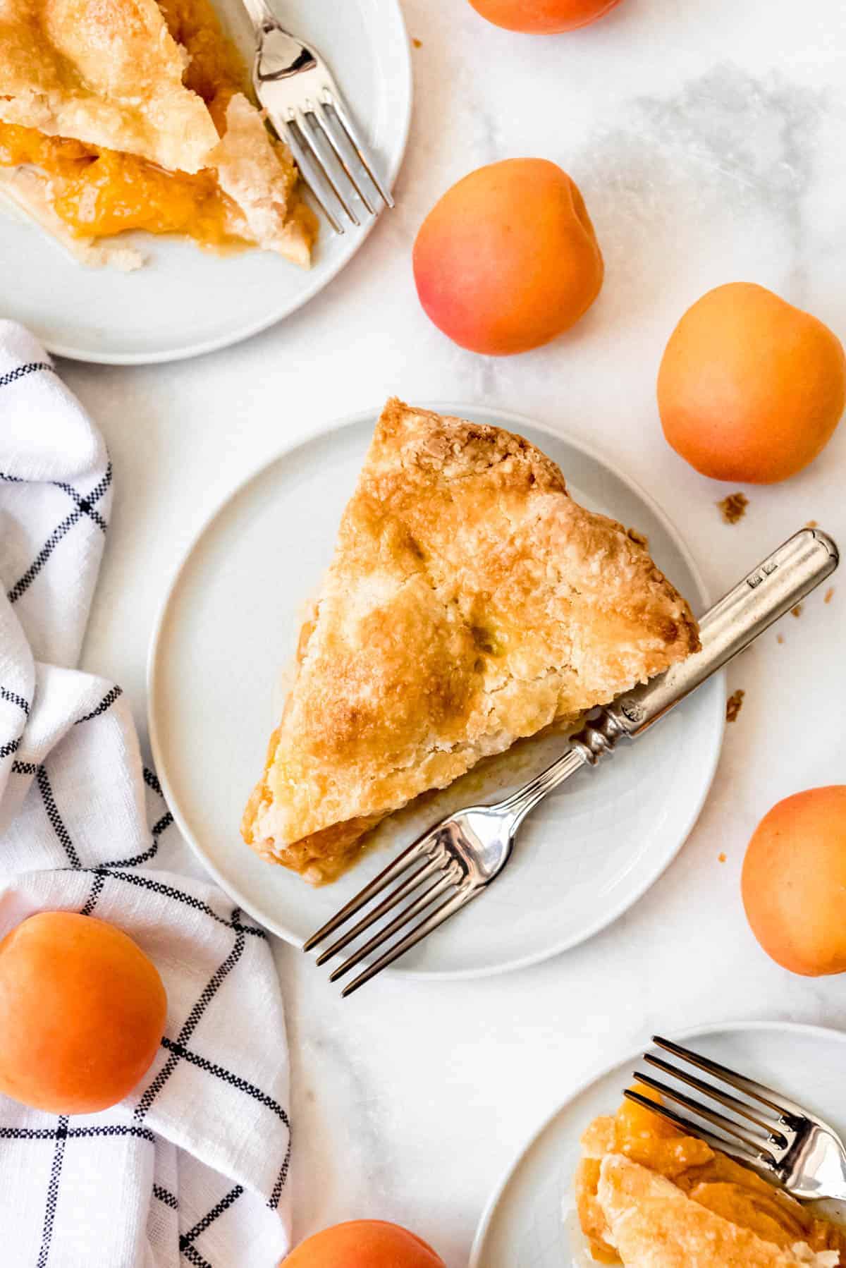 a slice of homemade apricot pie on a plate with a fork next to some fresh apricots