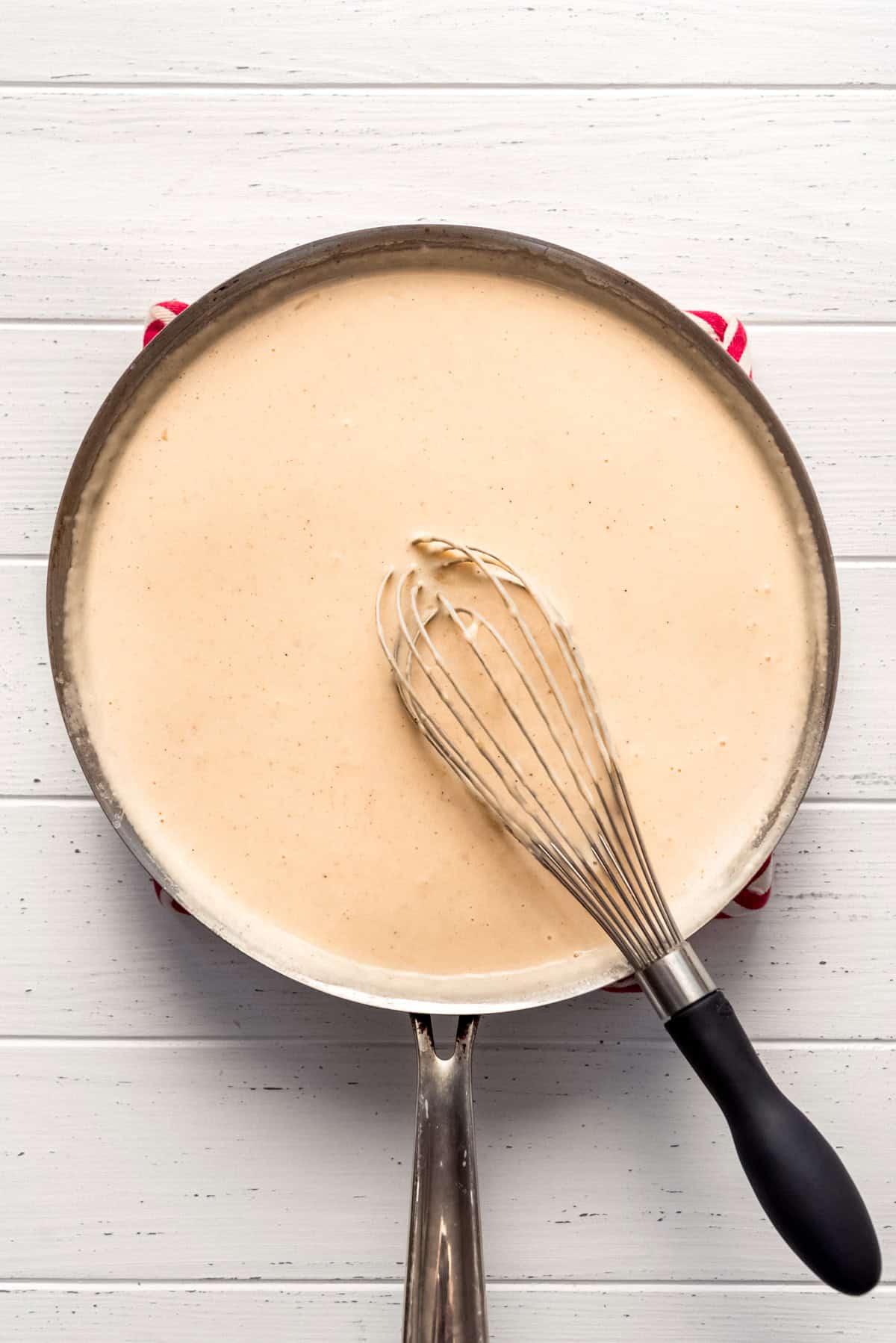 a homemade cheesy sauce in a large pan with a whisk in it