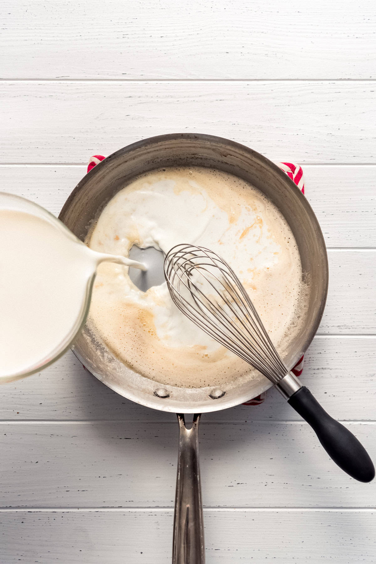 pouring milk into a large pan with roux