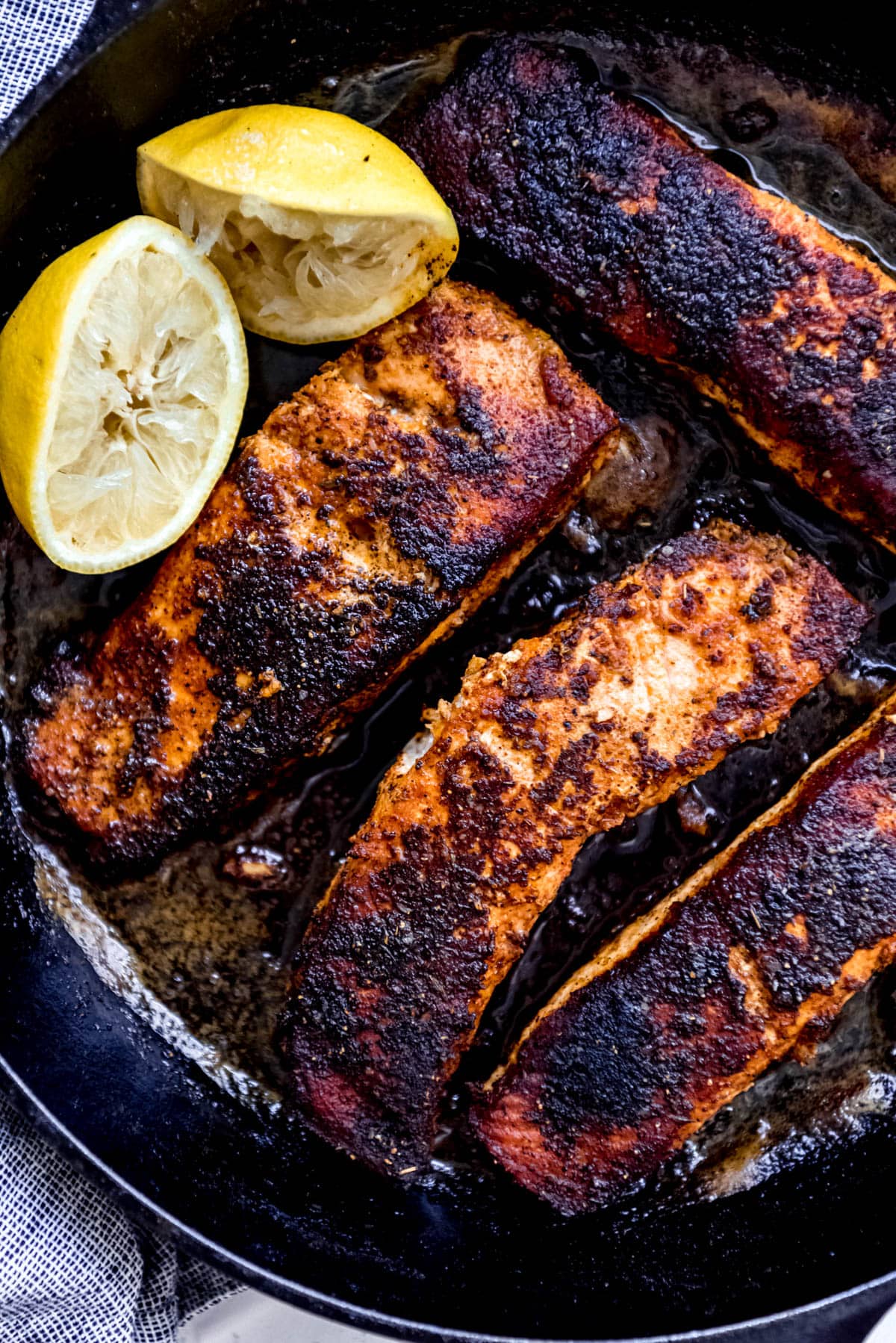 pan seared blackened salmon in cast iron skillet with lemon wedge
