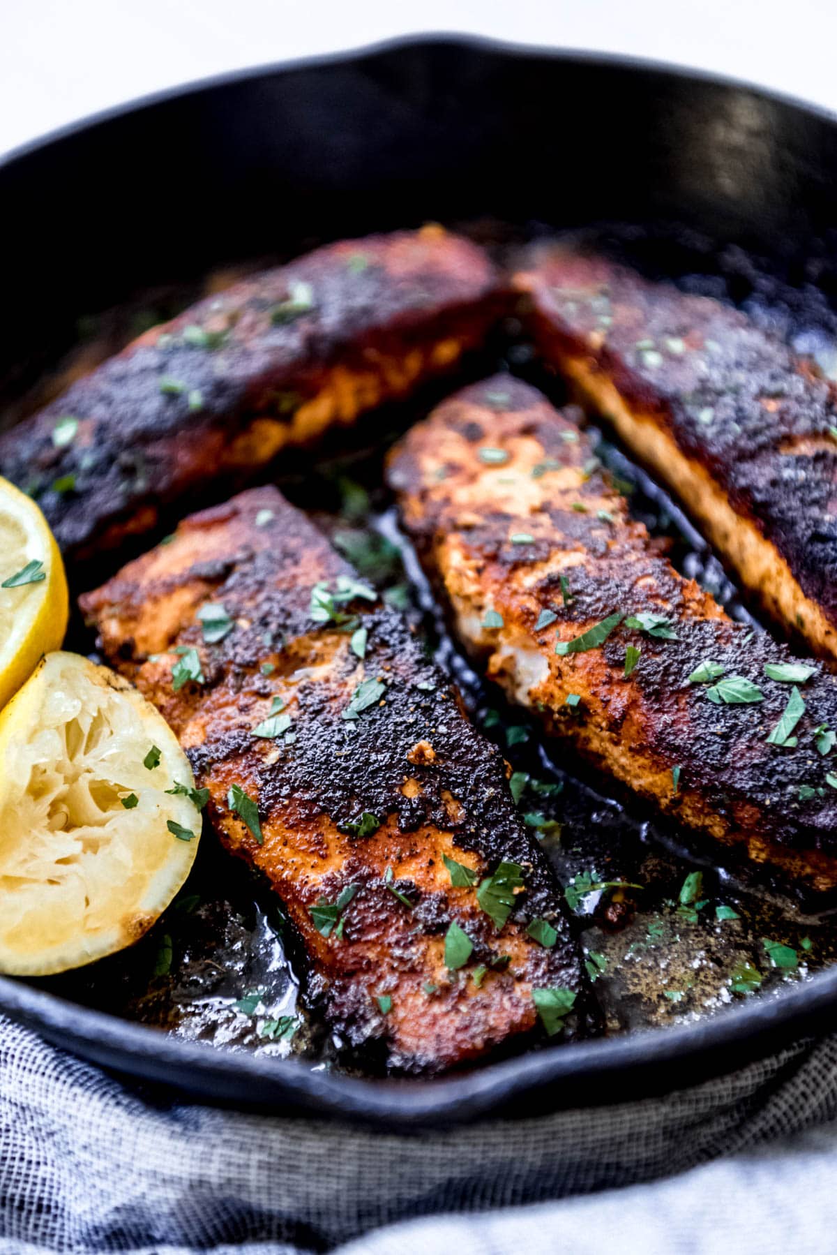 blackened salmon in cast iron skillet topped with fresh lemon juice and herbs