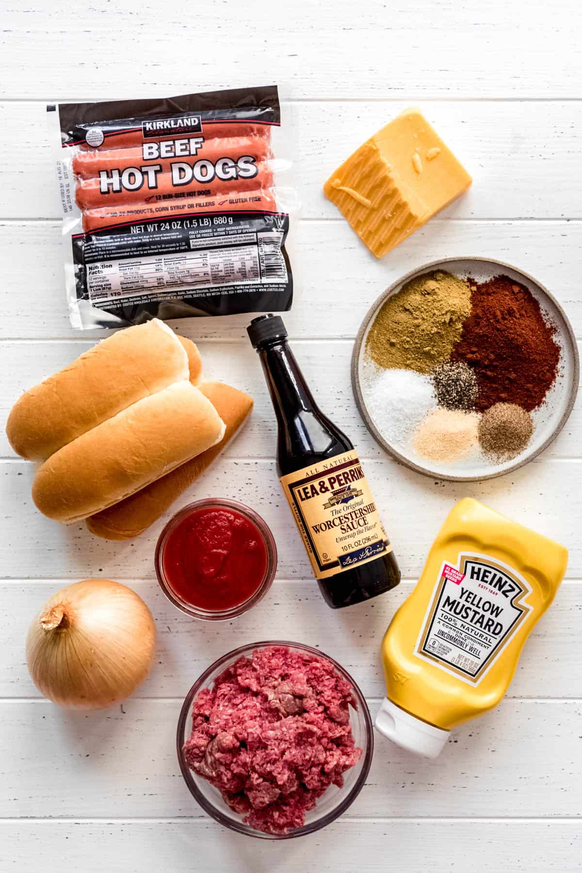 beef hot dogs, cheddar cheese, a plate of spices, hot dog buns, tomato sauce, Worcestershire sauce, mustard, an onion, ground beef