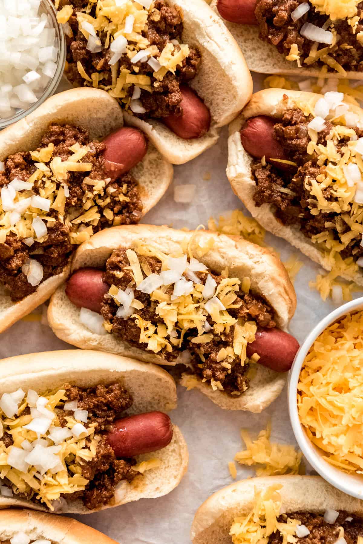 hot dogs on buns covered in meat sauce, shredded cheese, and onions
