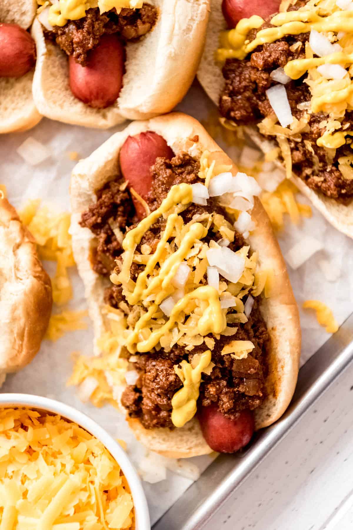 A coney island hot dog topped with chopped onions mustard and cheese on a baking sheet