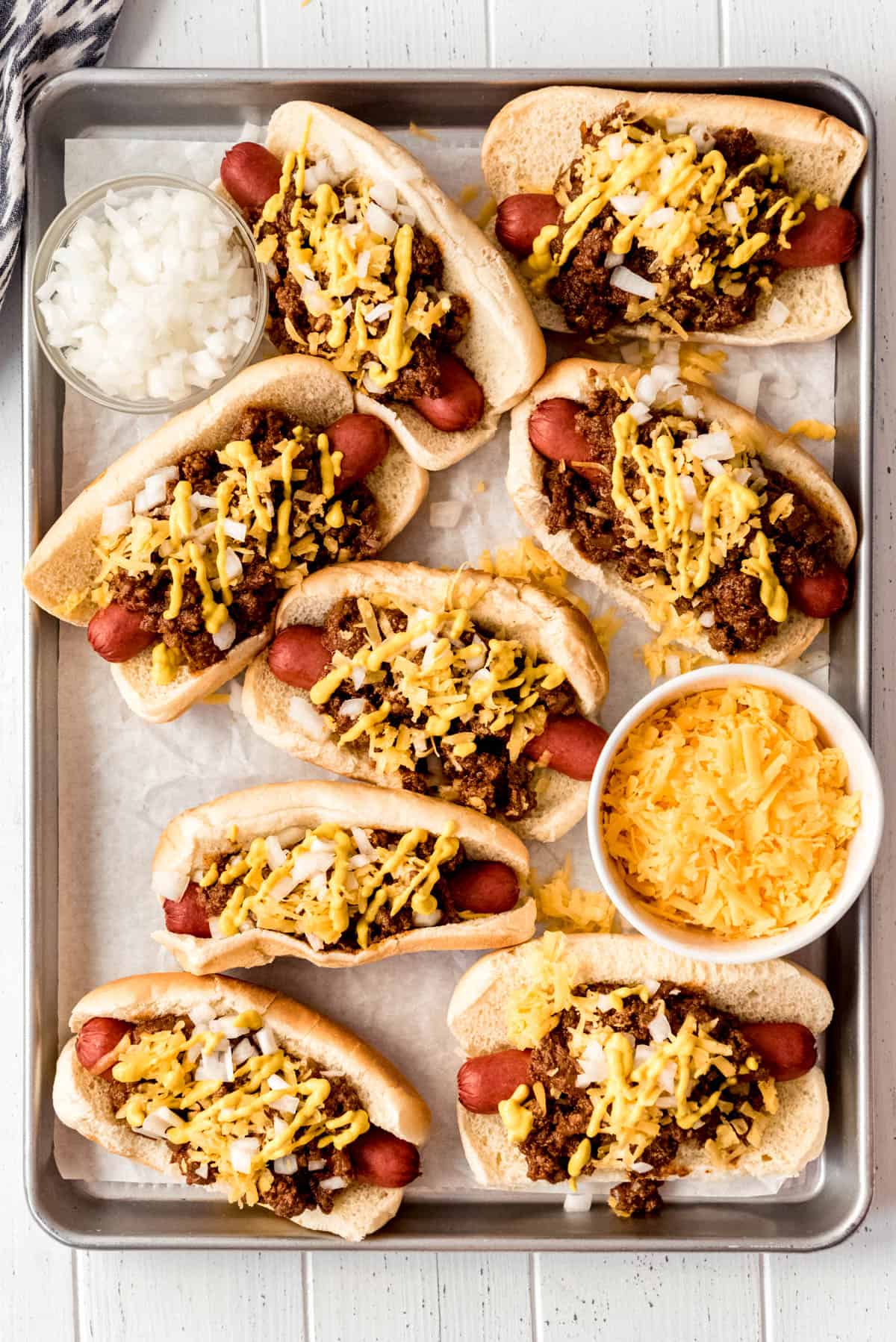 Overhead view of hot dogs in buns and topped with meat sauce, diced onions and shredded cheddar cheese. 