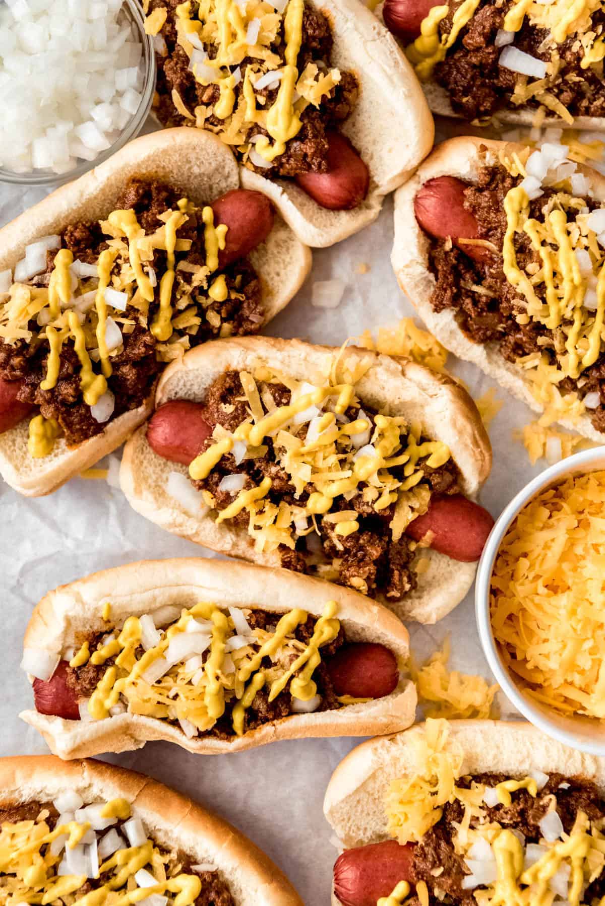 Coney Dogs topped with cheese and mustard on parchment paper
