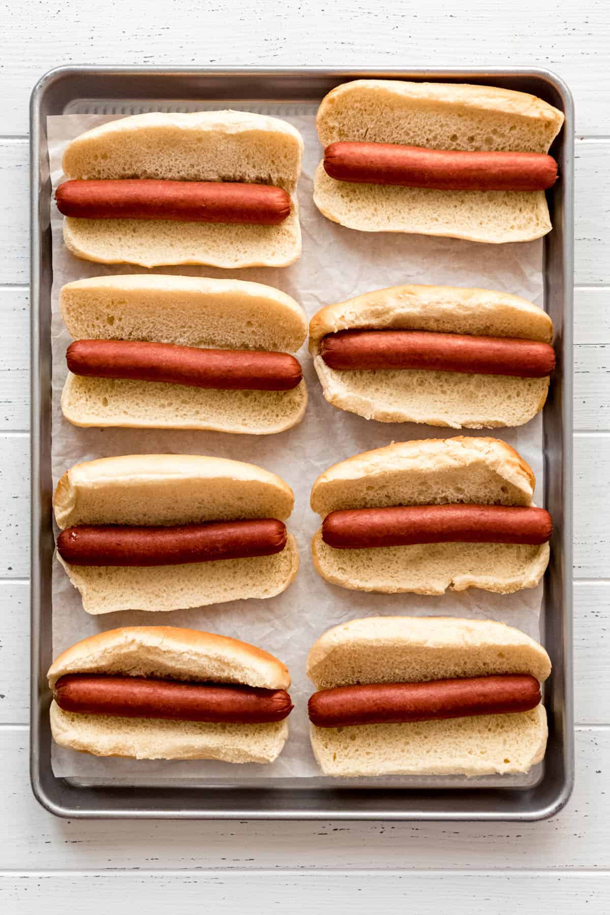 Hot dogs are placed in warmed buns, and set on a parchment lined baking sheet. 