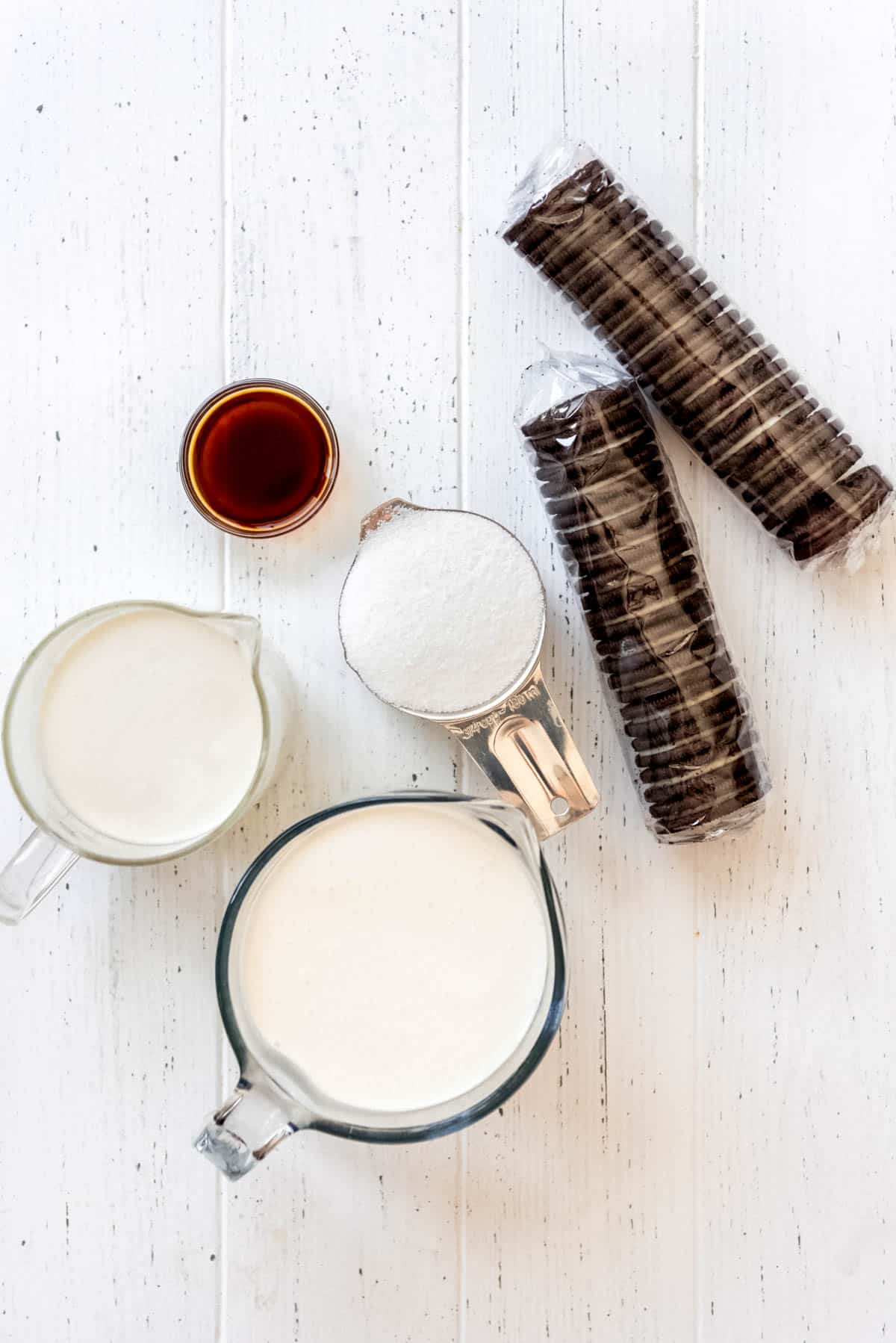 measuring cups of milk, heavy cream, sugar, vanilla extract and packages of Oreos on a white table