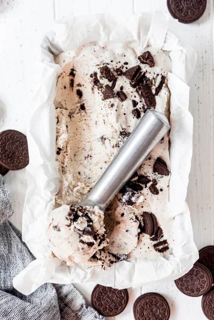 cookies and cream ice cream in a freezer safe container scooped out with an ice cream scoop on a white table