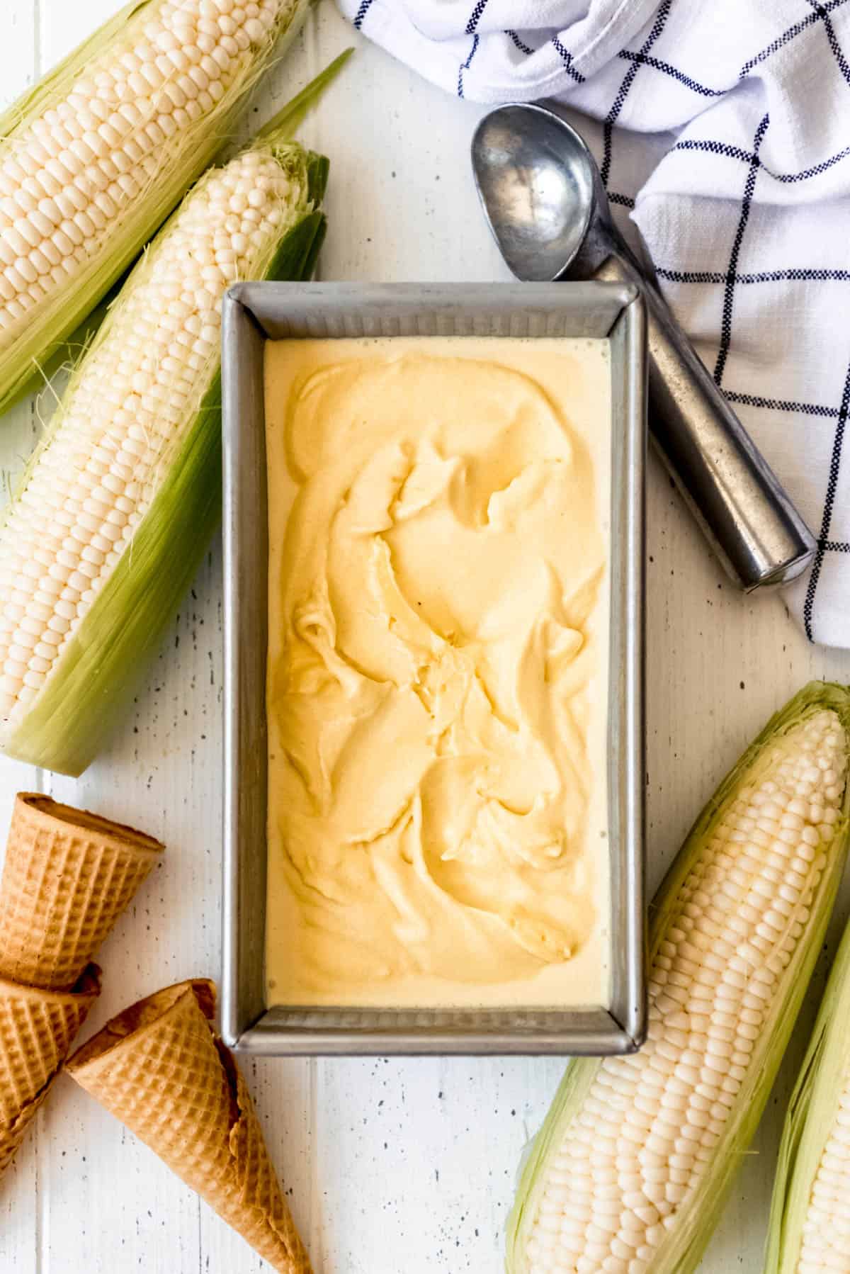 a bread pan filled with corn ice cream next to corn on the cob and sugar cones