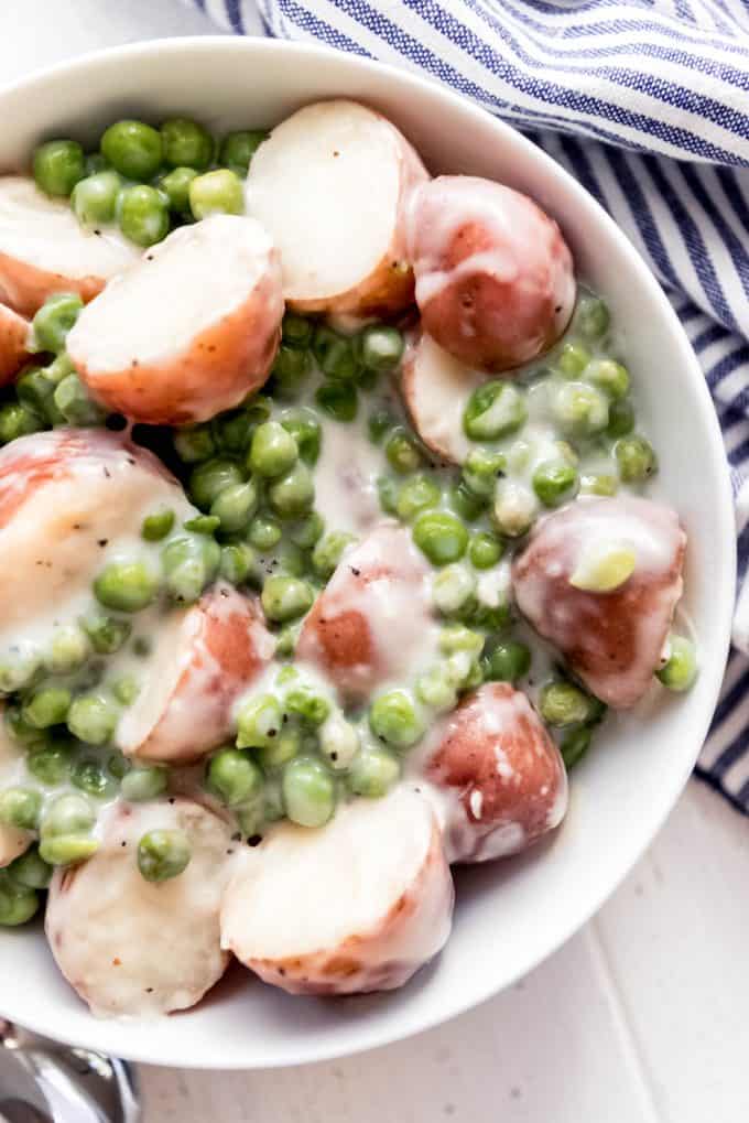 a close-up image of creamed peas and potatoes in a white bowl