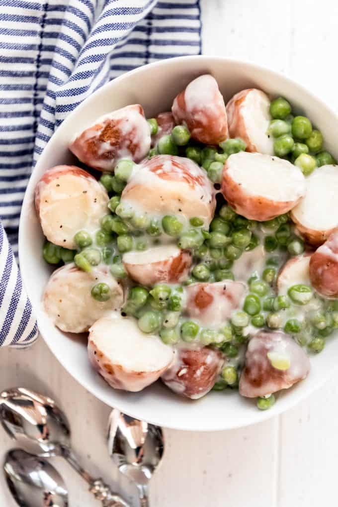 a white serving bowl of creamed peas and potatoes