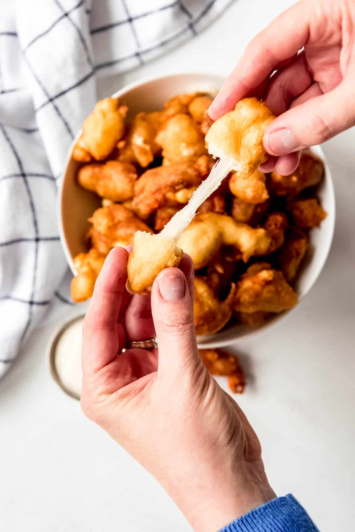 hands stretching apart a fried cheese curd