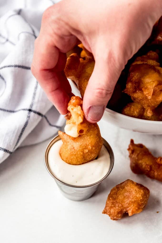 a hand dipping a fried cheese curd into a bowl of ranch dipping sauce