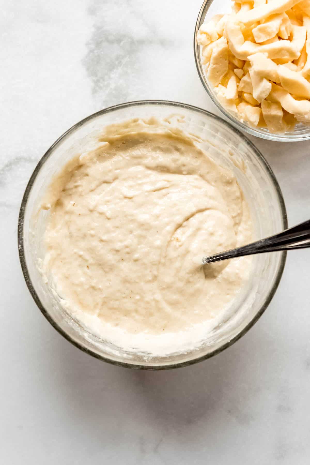 Batter for frying cheese curds is blended in a clear glass bowl. A smaller bowl containing cheese curds is visible in the corner of the photo. 