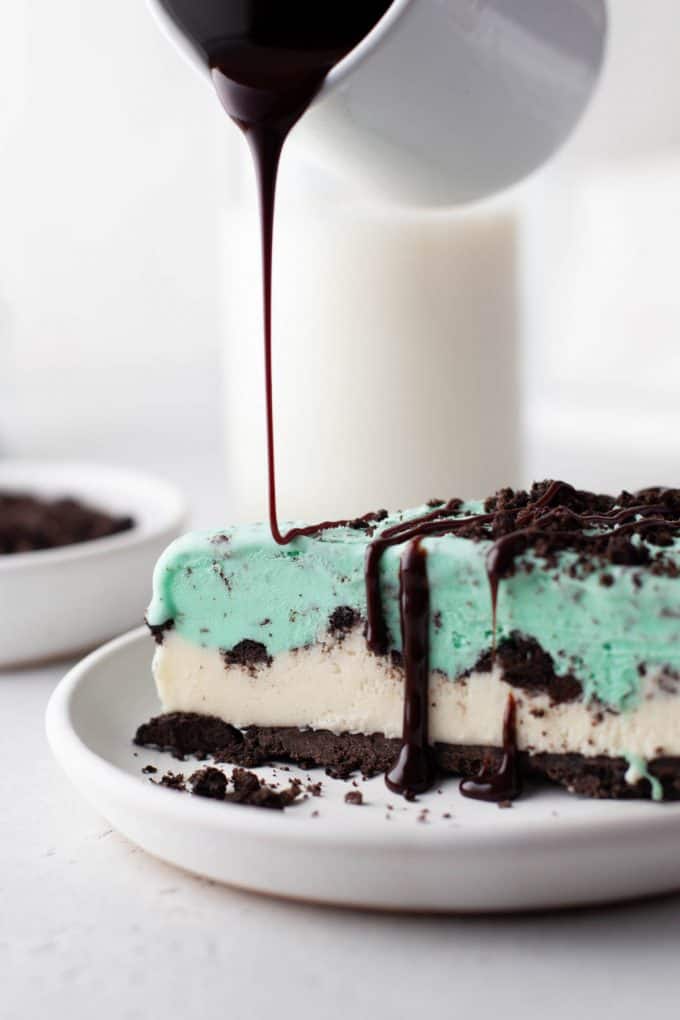 chocolate syrup being poured from a white pitchen on to a slice of grasshopper ice cream pie