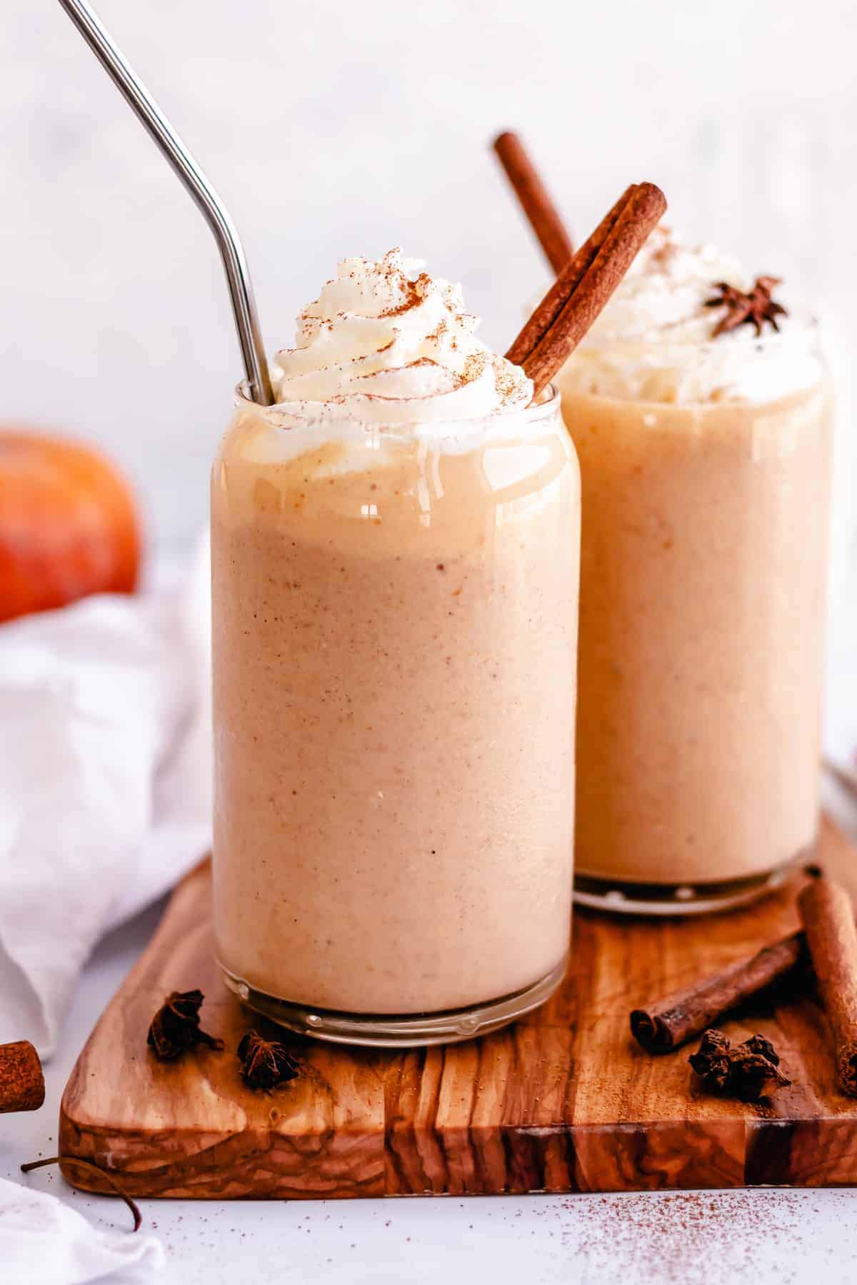 two glasses of pumpkin pie smoothie with whipped cream and a cinnamon stick. 
