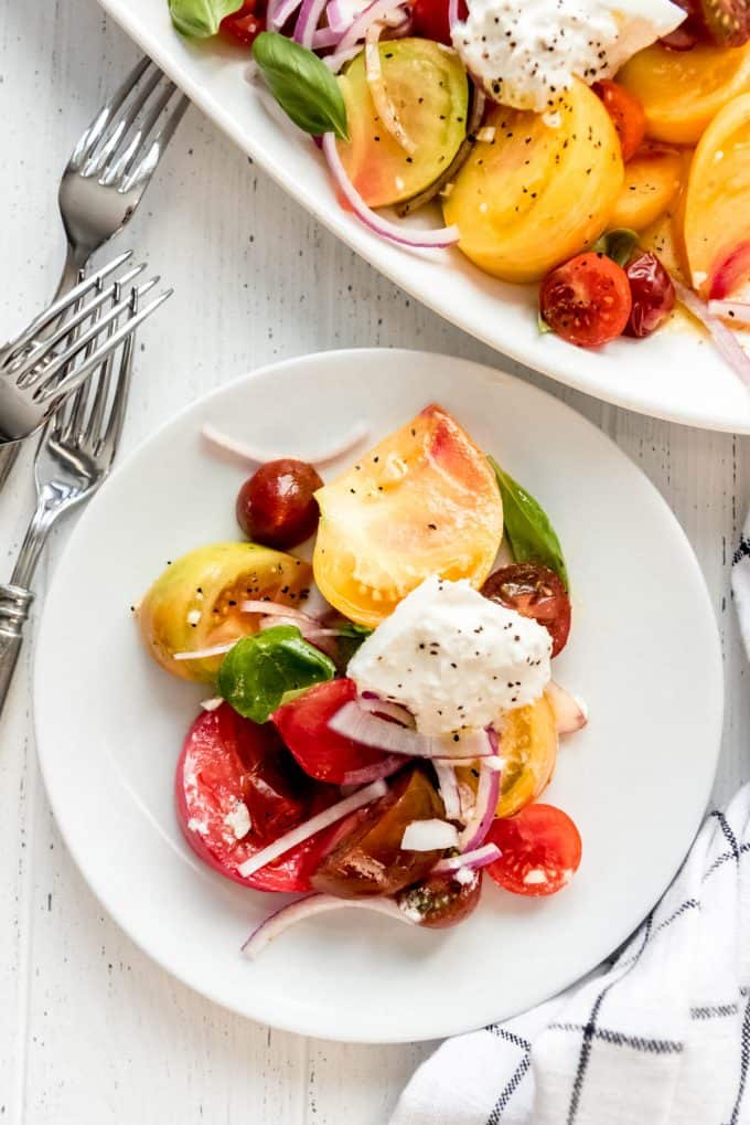 a white plate with a serving of fresh heirloom tomatoes, burrata cheese, and a simple dressing