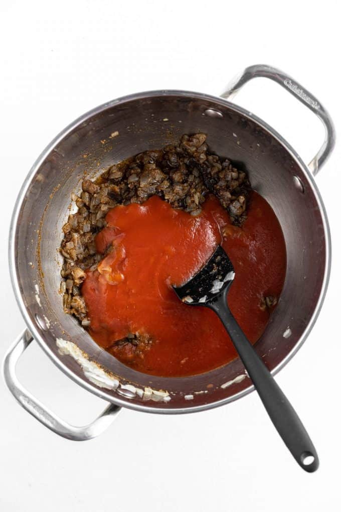 Adding tomato sauce to vegetables in a large pot.