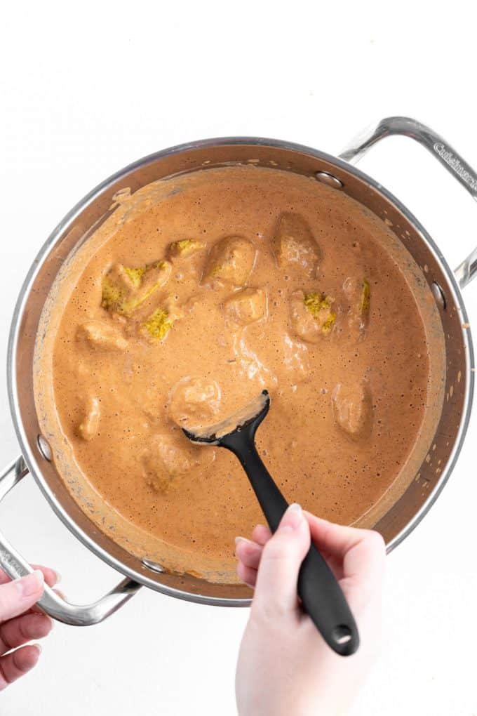 Stirring chunks of cooked chicken into a creamy spiced curry sauce.