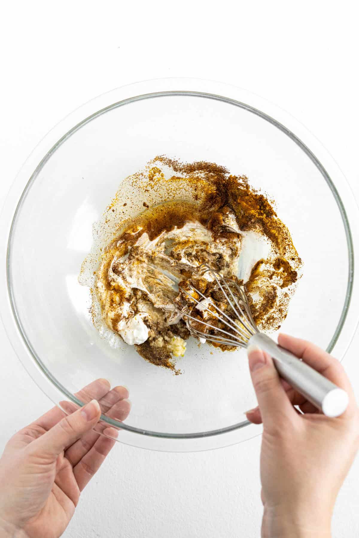 Whisking butter chicken marinade ingredients together in a glass bowl with a whisk.