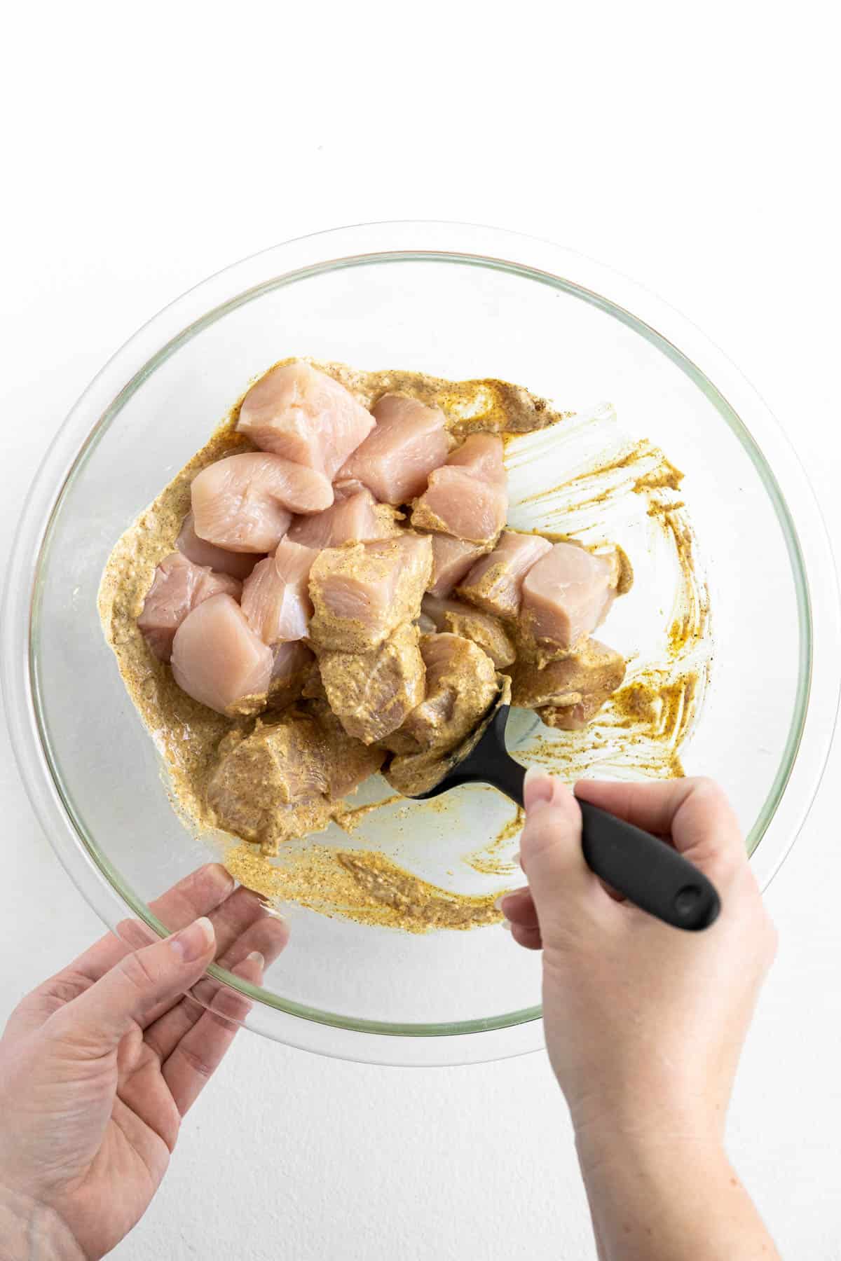 Adding chunks of uncooked chicken to marinade in a glass bowl.