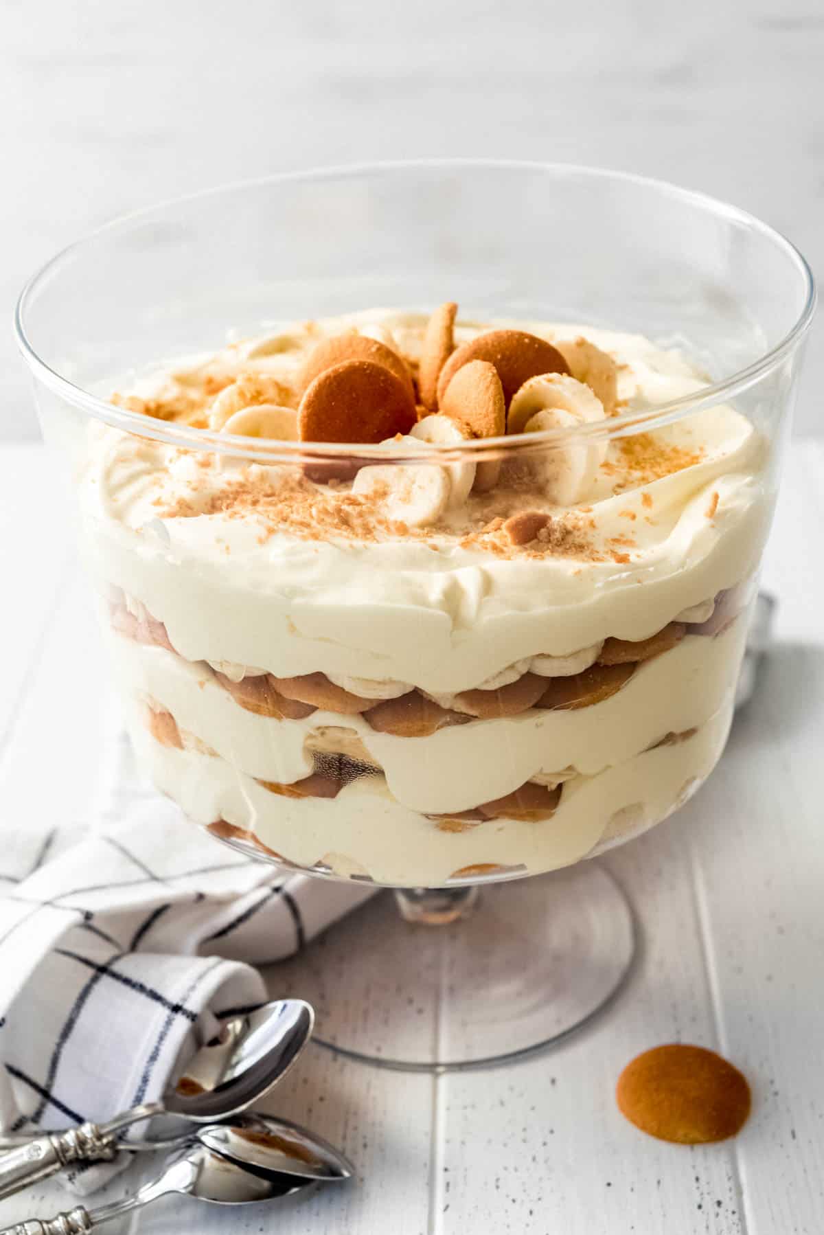Magnolia Bakery Banana Pudding layered in a trifle dish on a white table with a dish towel and a serving spoon