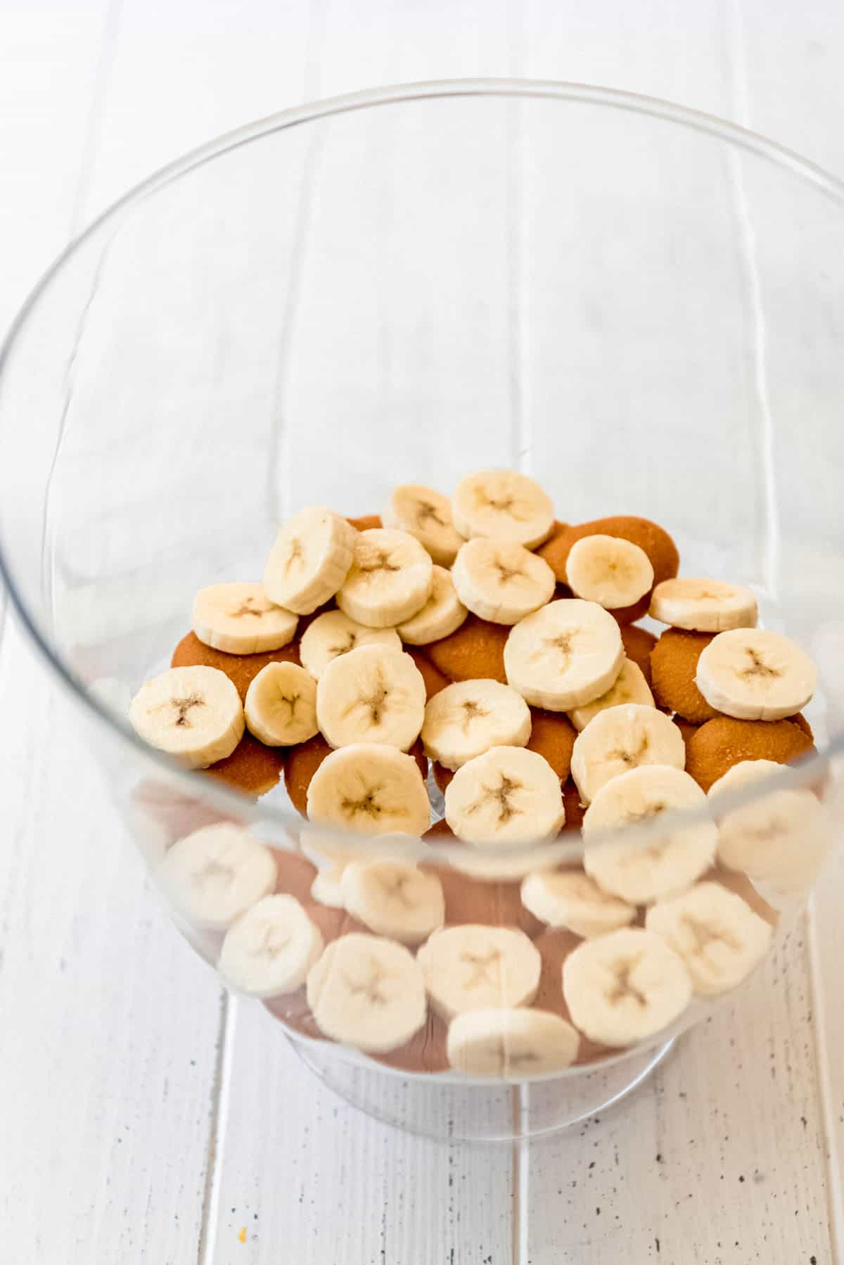 Layering sliced bananas on top of Nilla wafers in a trifle dish.