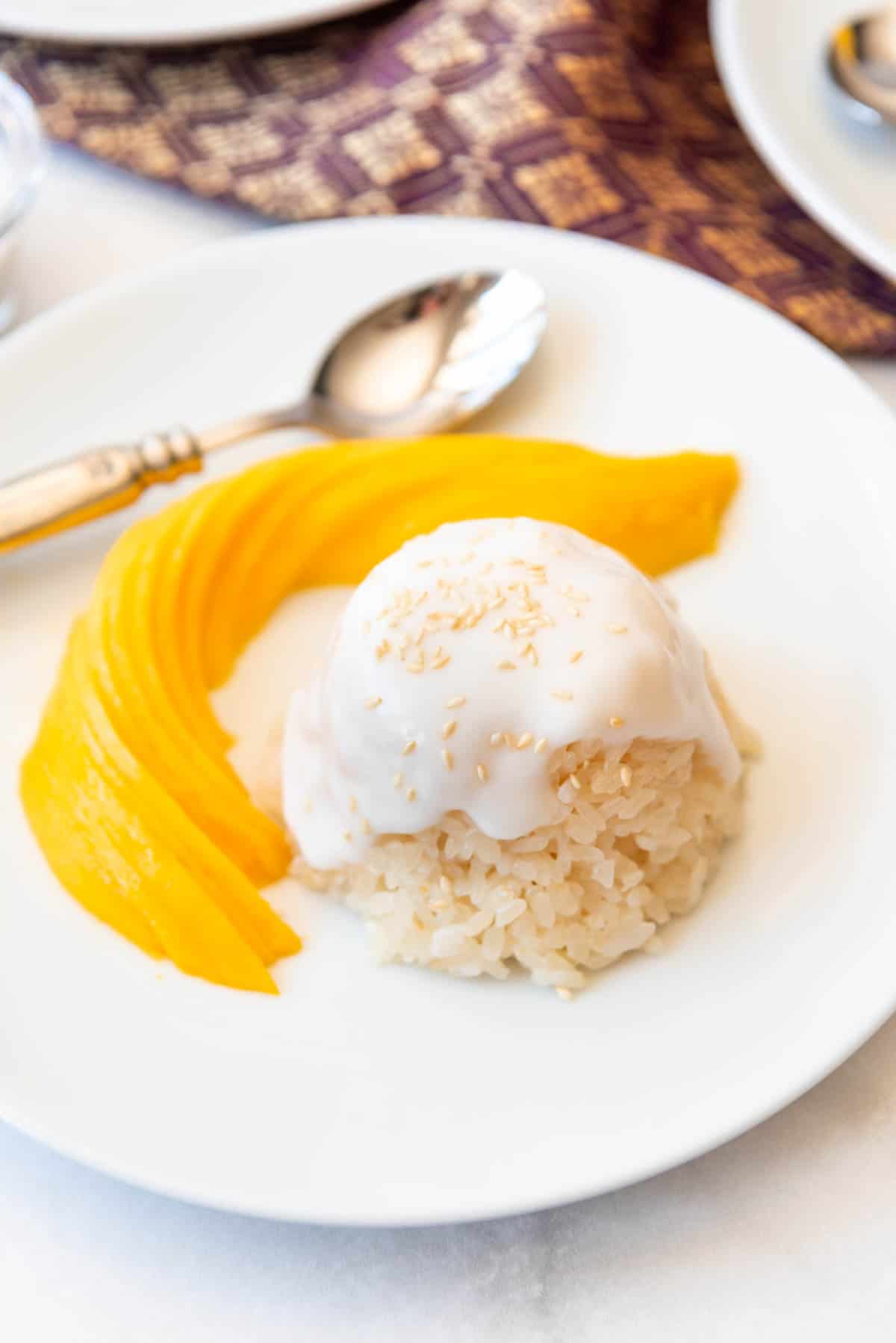 Close up of mango sticky rice in a dome on a white plate with a thinky sliced and fanned mango next to it. 