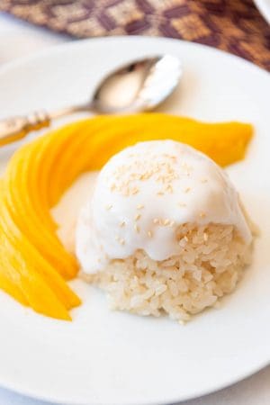 Close up of mango sticky rice in a dome on a white plate with a thinky sliced and fanned mango next to it.