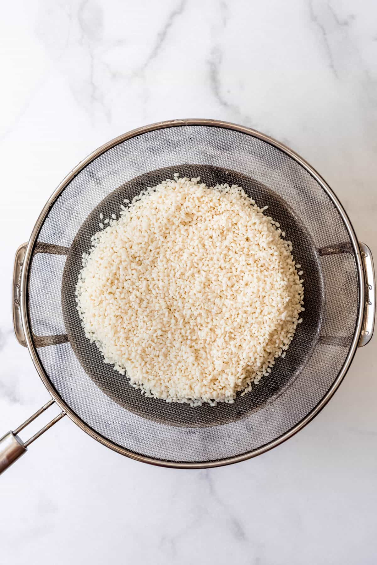Top view of rice in a strainer sitting on top of a large pot of water. 