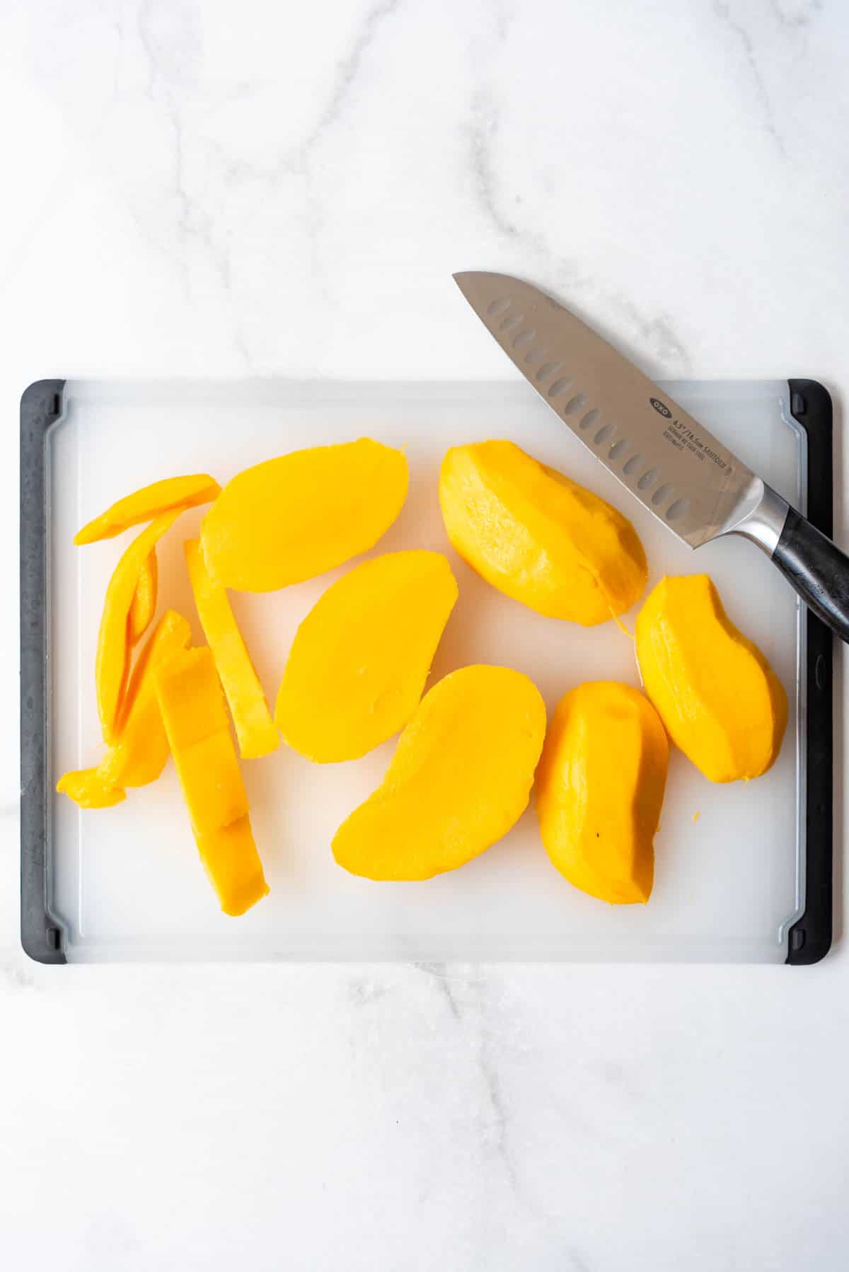 Top view of a sliced mango on a white chopping board with a sharp knife. 