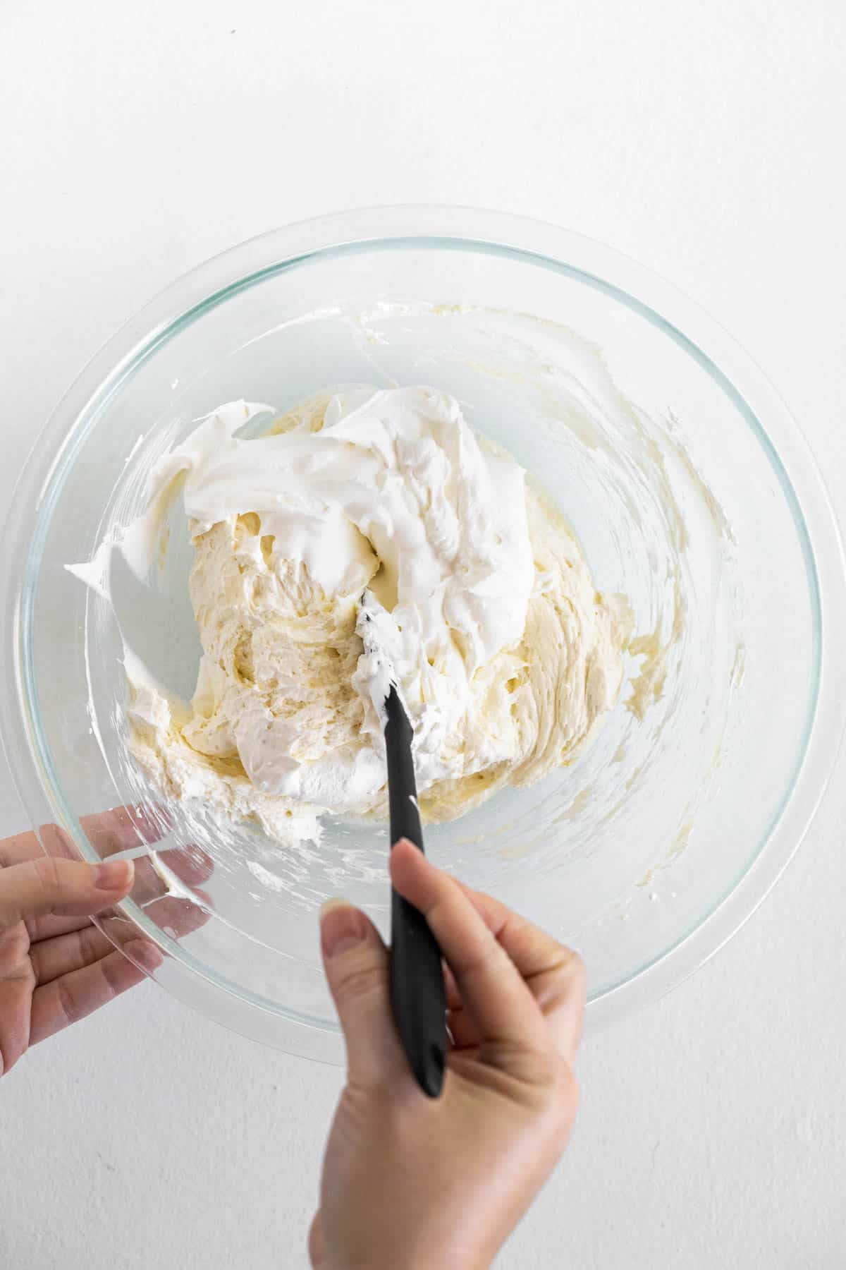 A hand is stirring the cream cheese mixture and whipped cream together. 