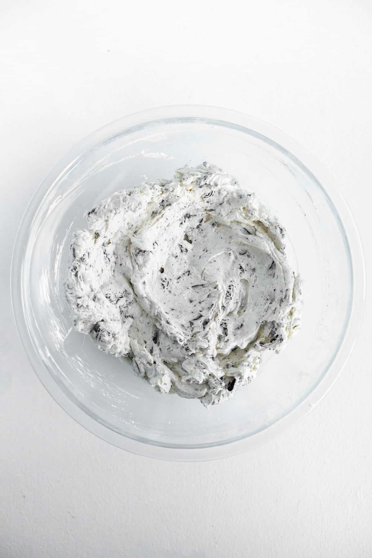 Oreo dip mixture is fully blended and resting in the bottom of a clear glass mixing bowl. 