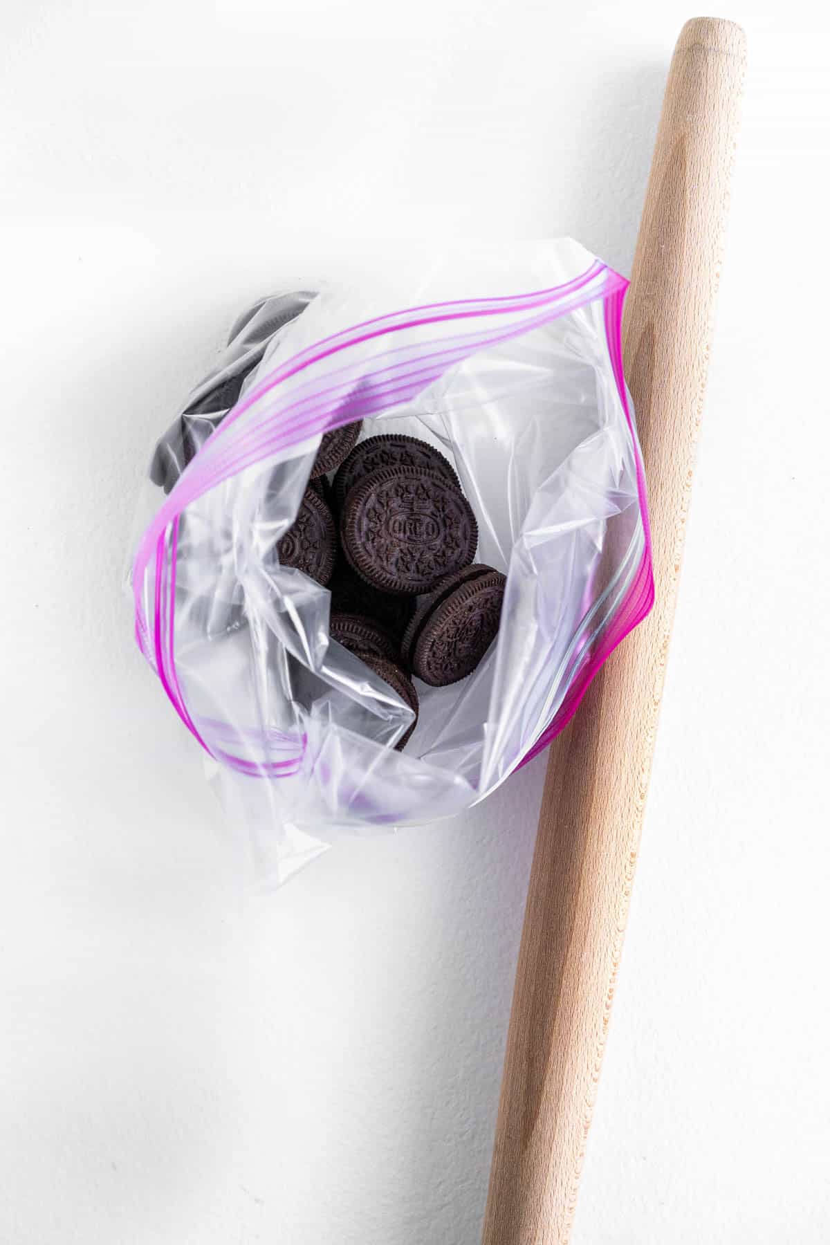 Whole Oreos are placed in a zip top bag, next to a wooden rolling pin. 