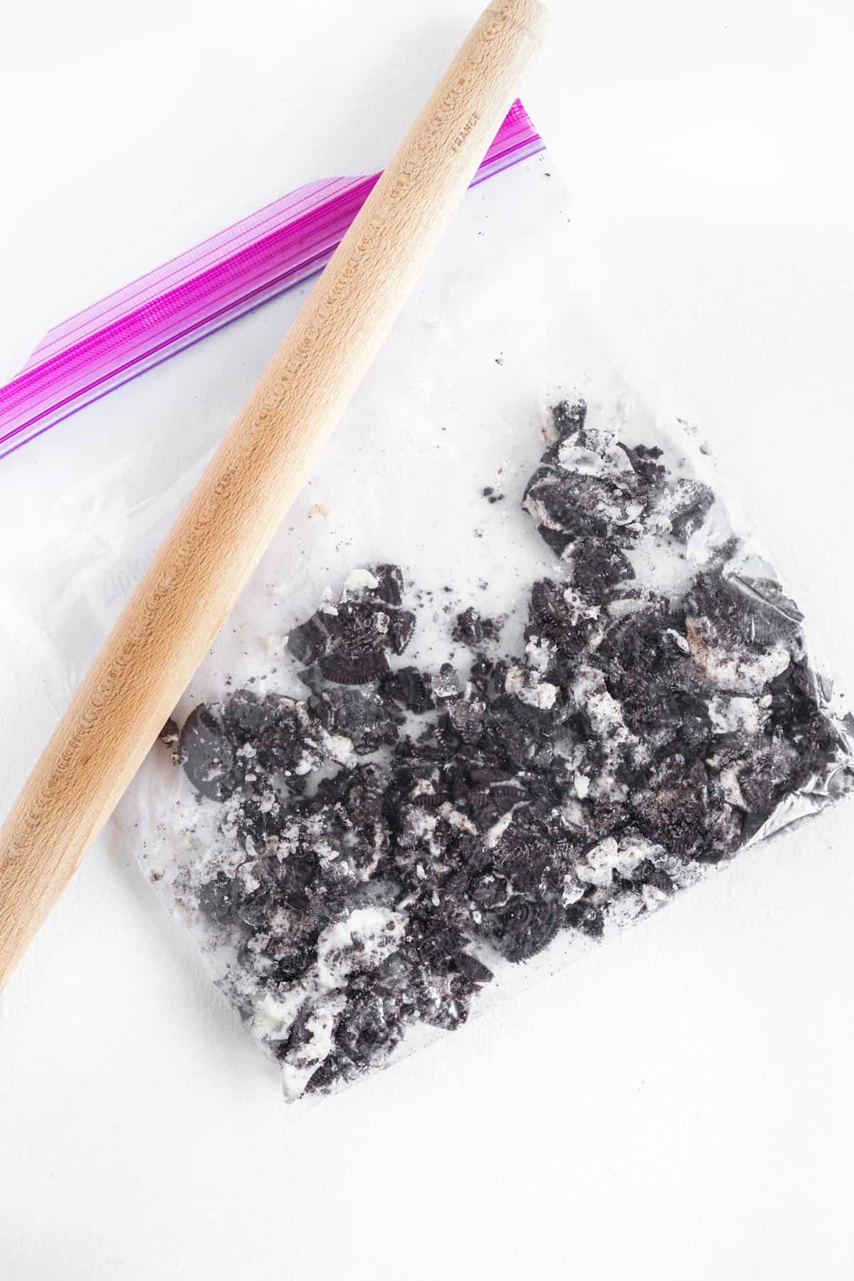 A wooden rolling pin sits on top of a bag of crushed Oreo cookies. 