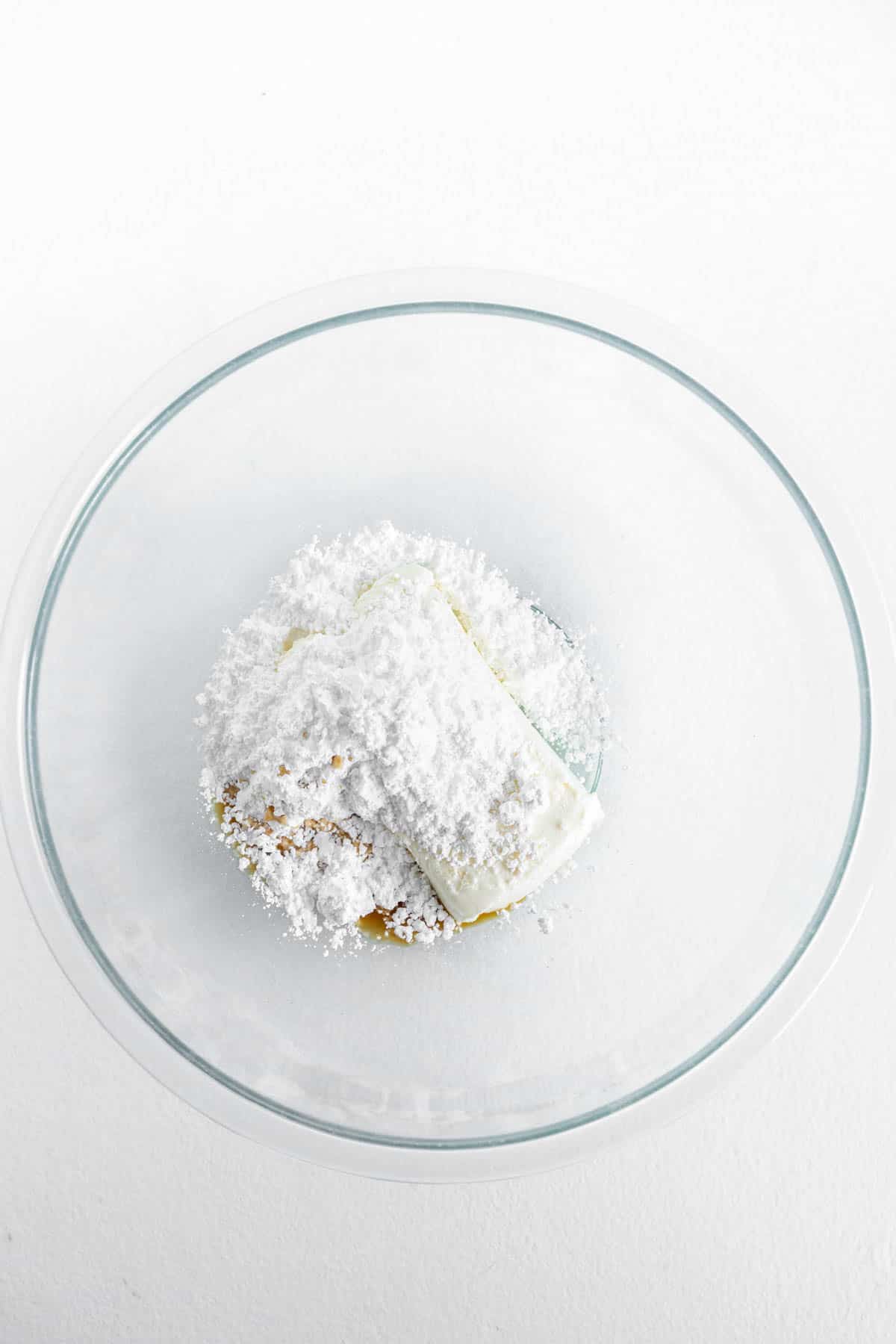 Softened cream cheese, powdered sugar and vanilla are placed in a clear glass mixing bowl. 