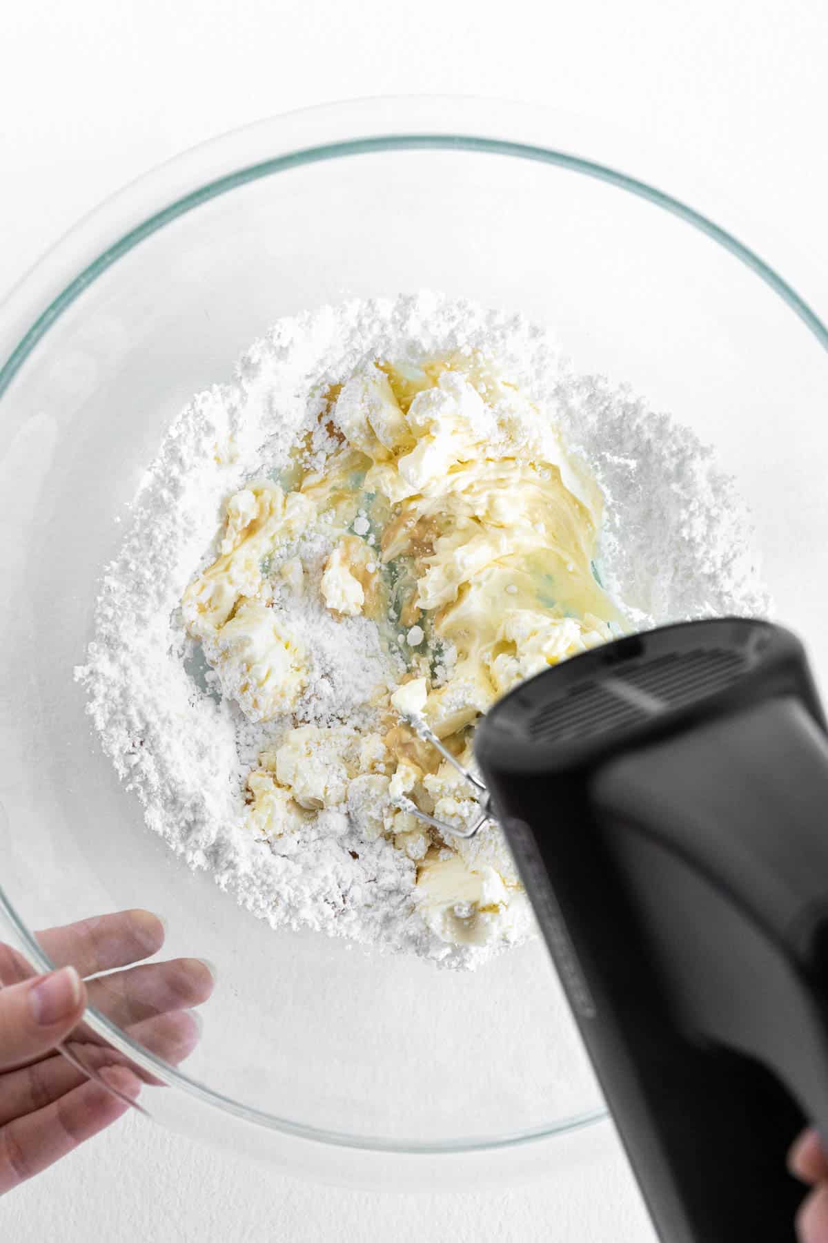 A hand mixer is blending the cream cheese and sugar mixture. 