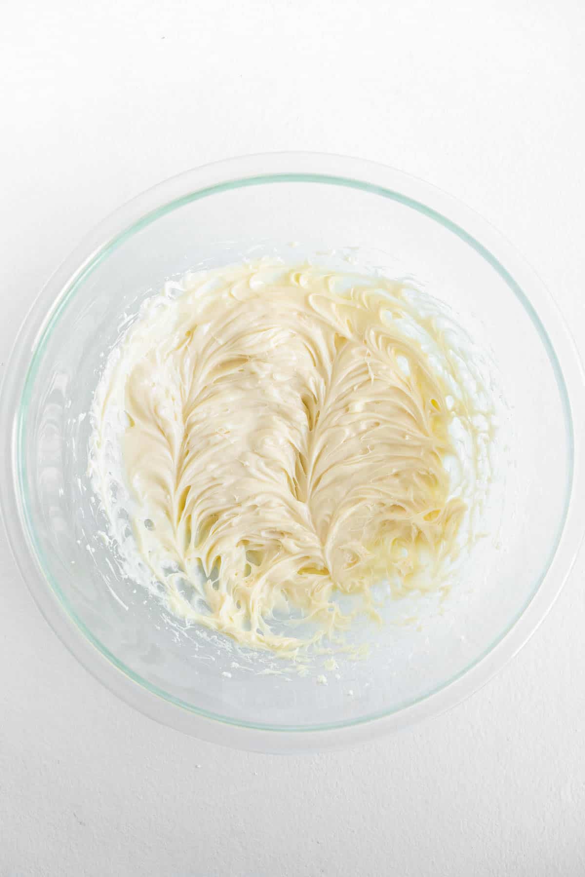 The cream cheese and powdered sugar mixture has been beaten and is visible in the bottom of a glass mixing bowl.