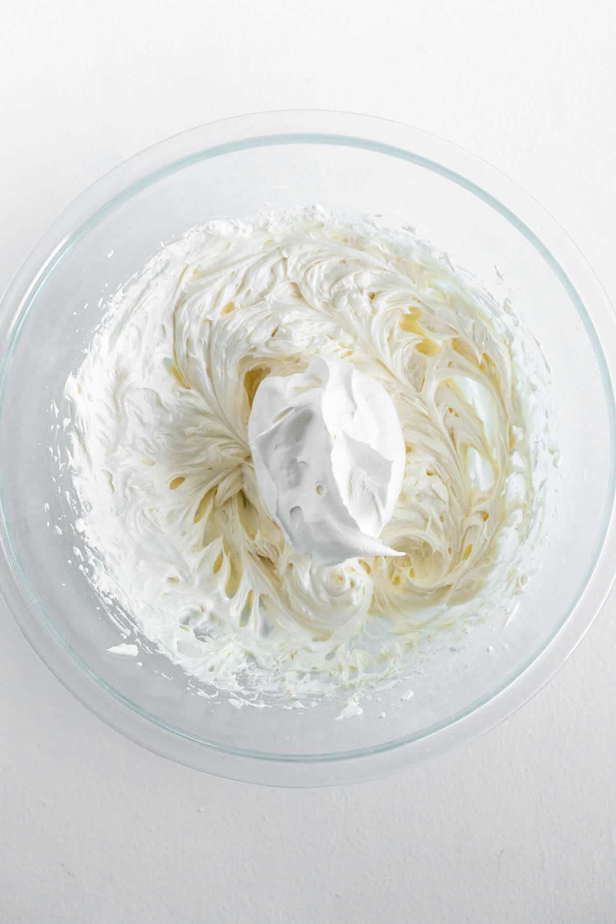 Whipped cream is added to the cream cheese mixture, preparing to be mixed. 