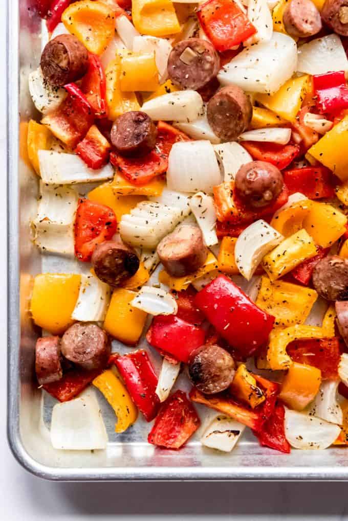 Sweet bell peppers, onions, and chicken apple sausages on a baking sheet.