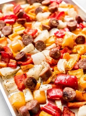 Roasted peppers, onions, and sausages on a baking sheet.