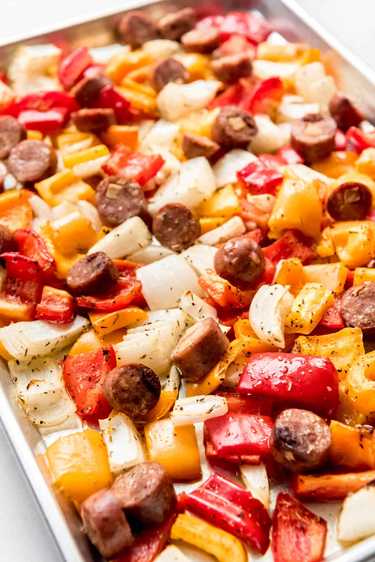 Roasted peppers, onions, and sausages on a baking sheet.