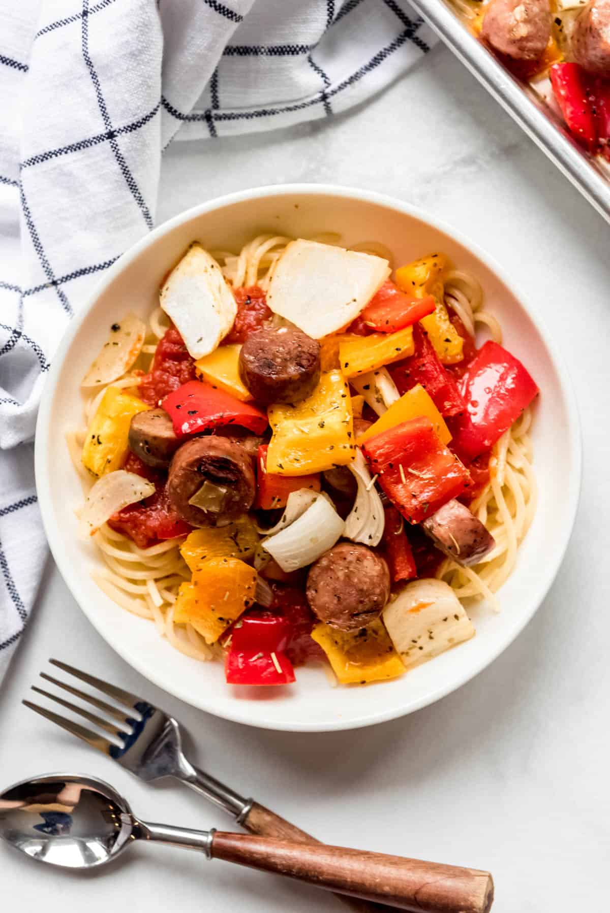 A bowl of pasta with sheet pan sausages, peppers, and onions on top.