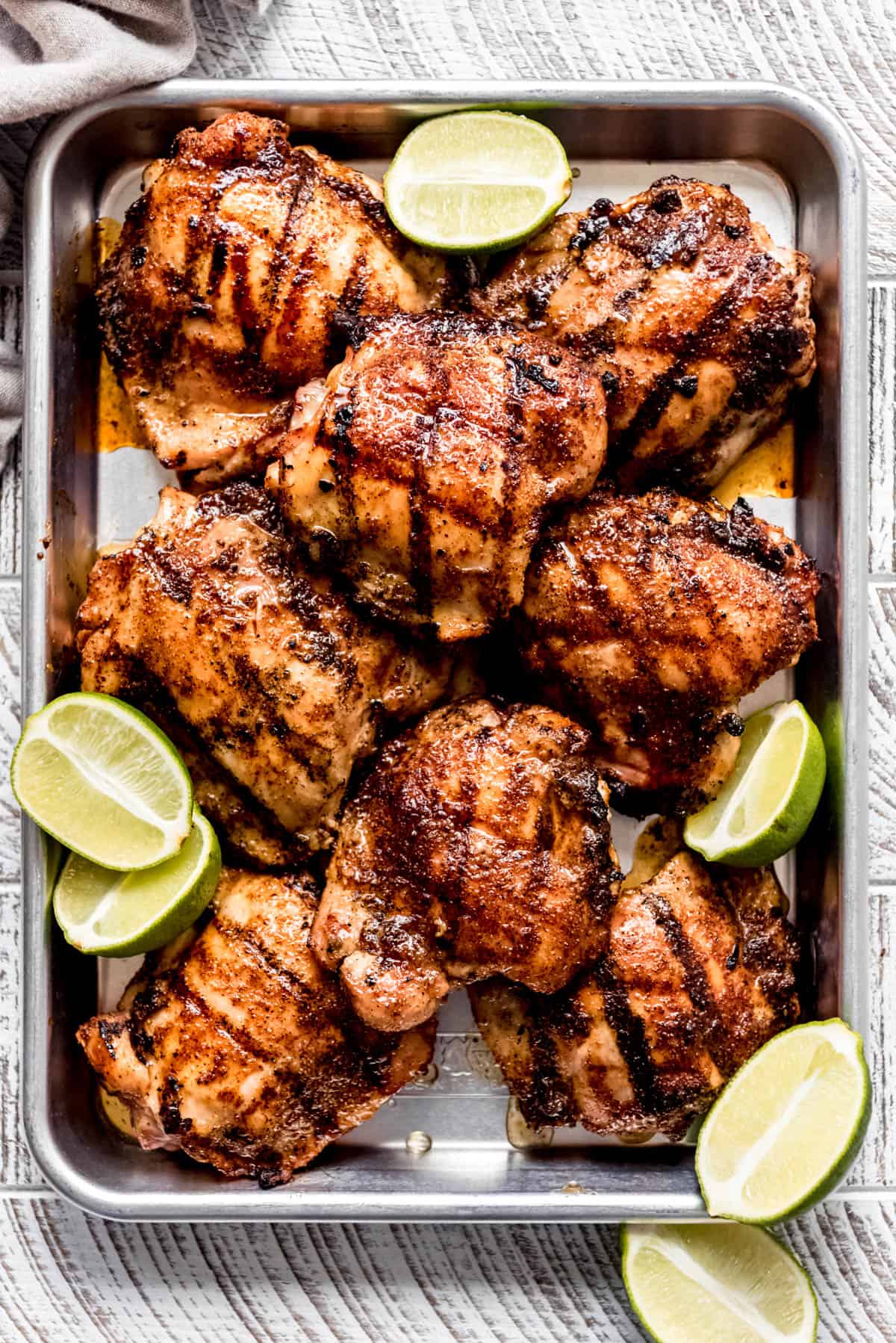 grilled chicken thighs on a baking sheet garnished with fresh limes