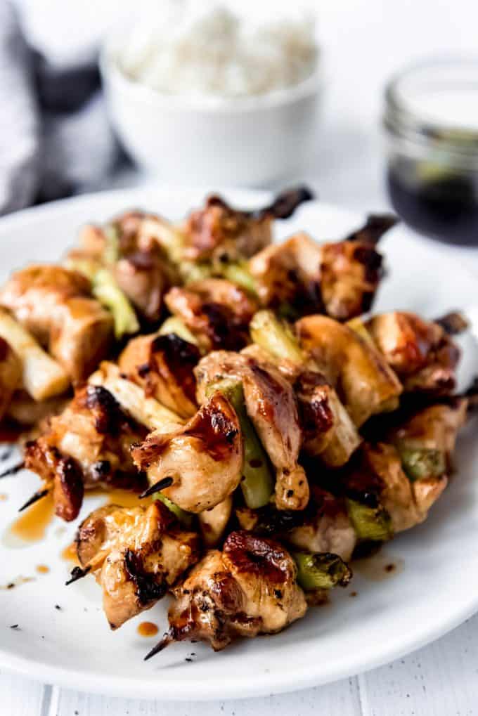 wooden skewers with grilled chicken and green onions on a white plate