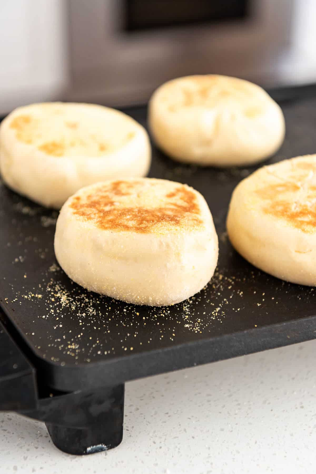 English muffins being cooked on a griddle.