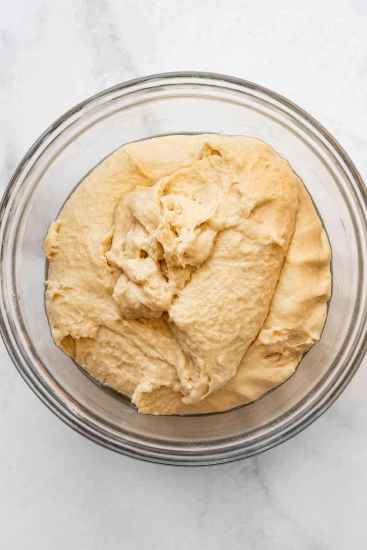 Kneaded english muffin dough in a glass bowl before rising.