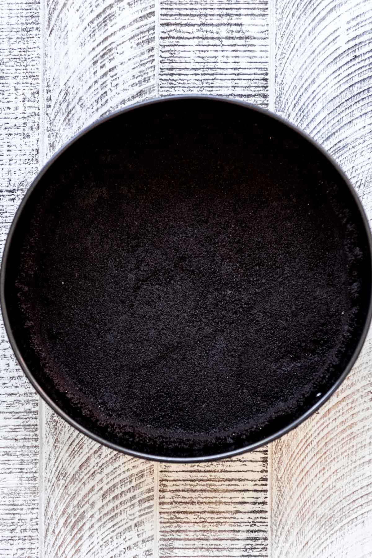 Oreo cookie crumbs are pressed in a cheesecake pan. 